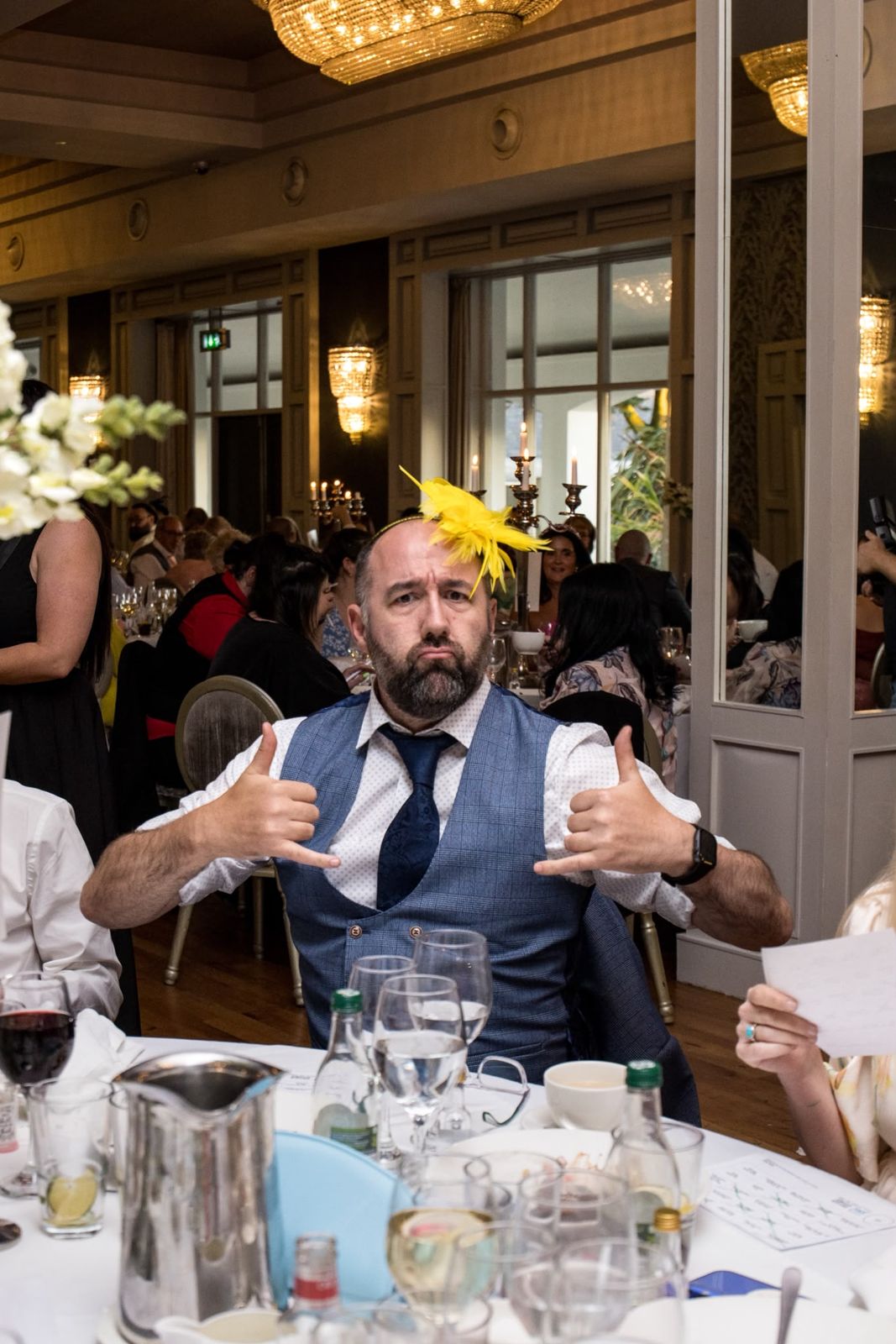 A wedding guest in a yellow fascinator throwing shapes at his table