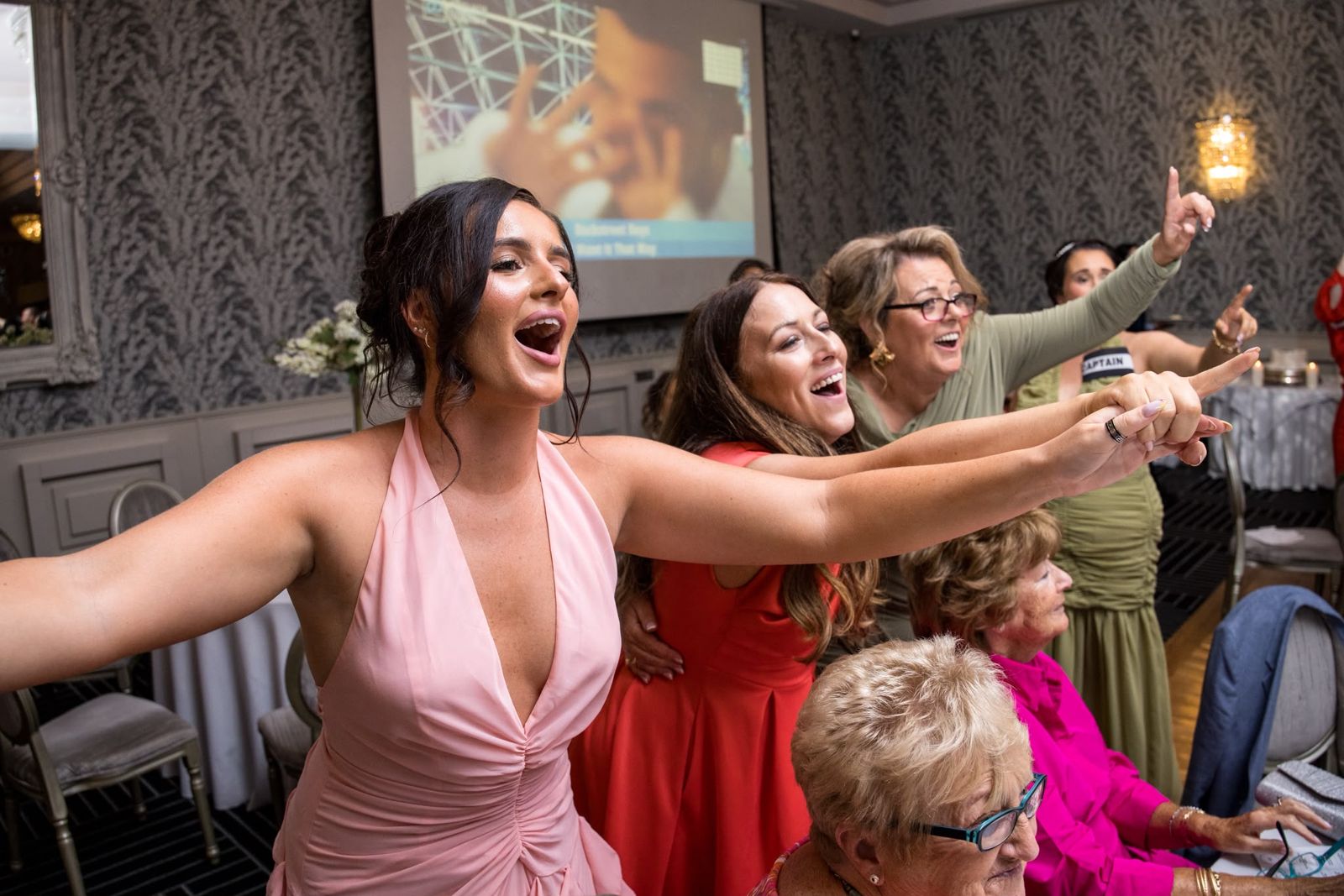 A table of wedding guests pointing and singing along