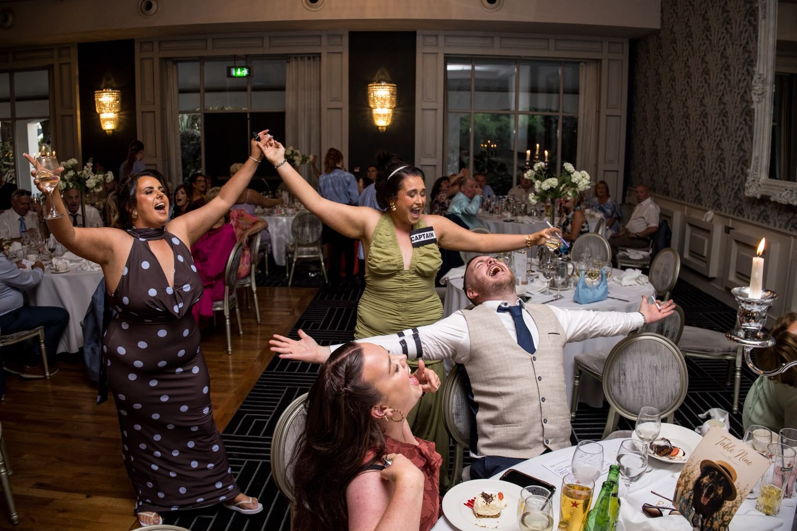 Guests up out of their seats, arms wide, singing between the tables